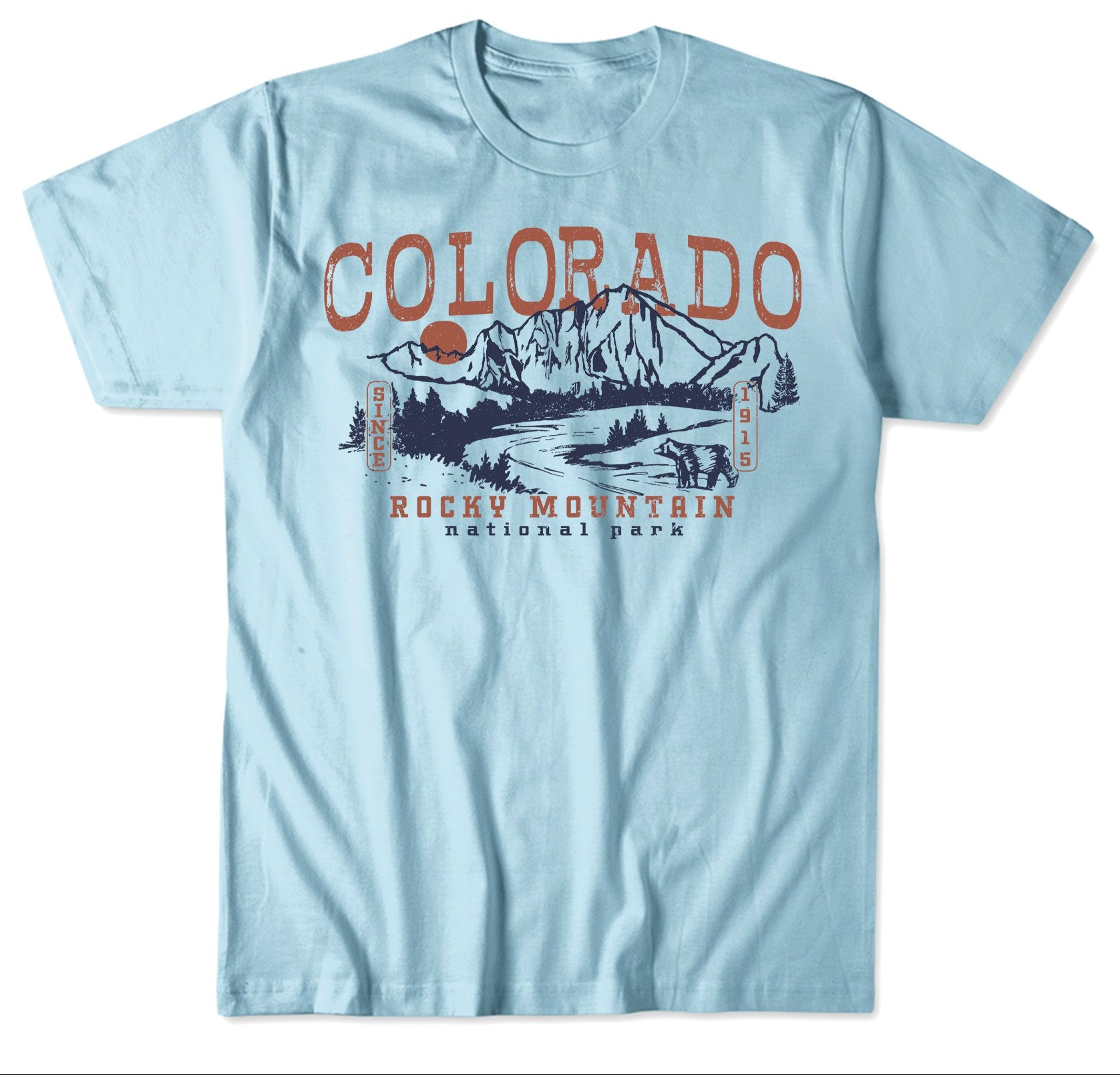 A light blue graphic t-shirt featuring a 'Colorado Rocky Mountain National Park' print in dark blue and rust orange. The image includes a color swatch at the top showing the light blue fabric and a portion of the graphic, with product code text 'HIGHLAND LONGS PEAK H21SLP-LM CPT4001 Light Blue' below.